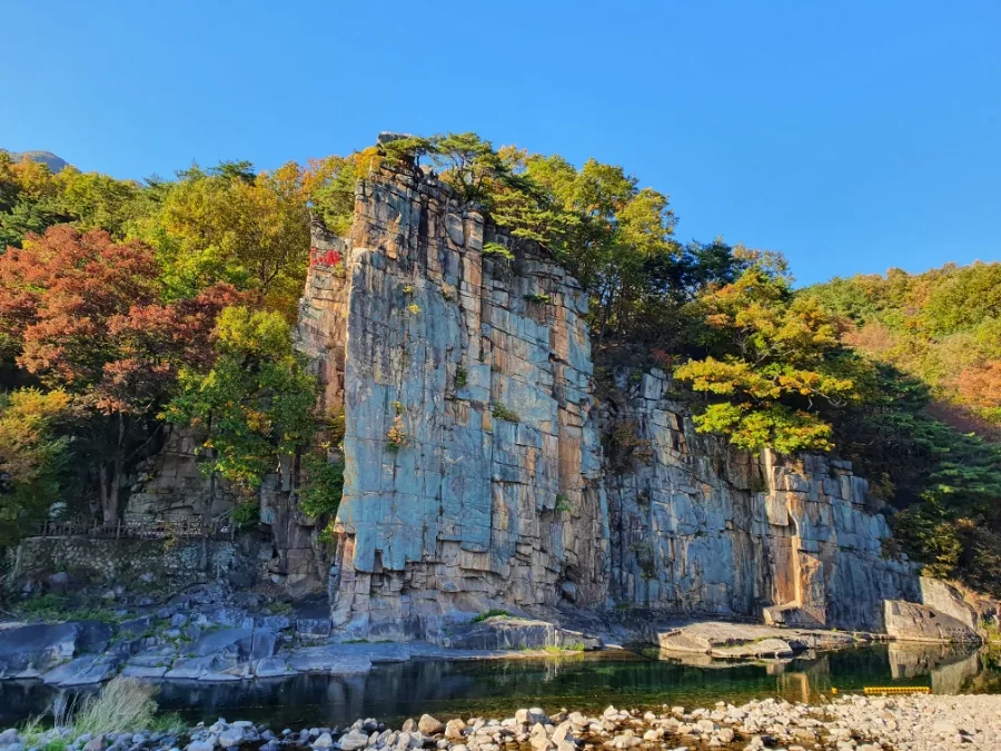 The grey rock wall of Sainam above shallow water and pale stones