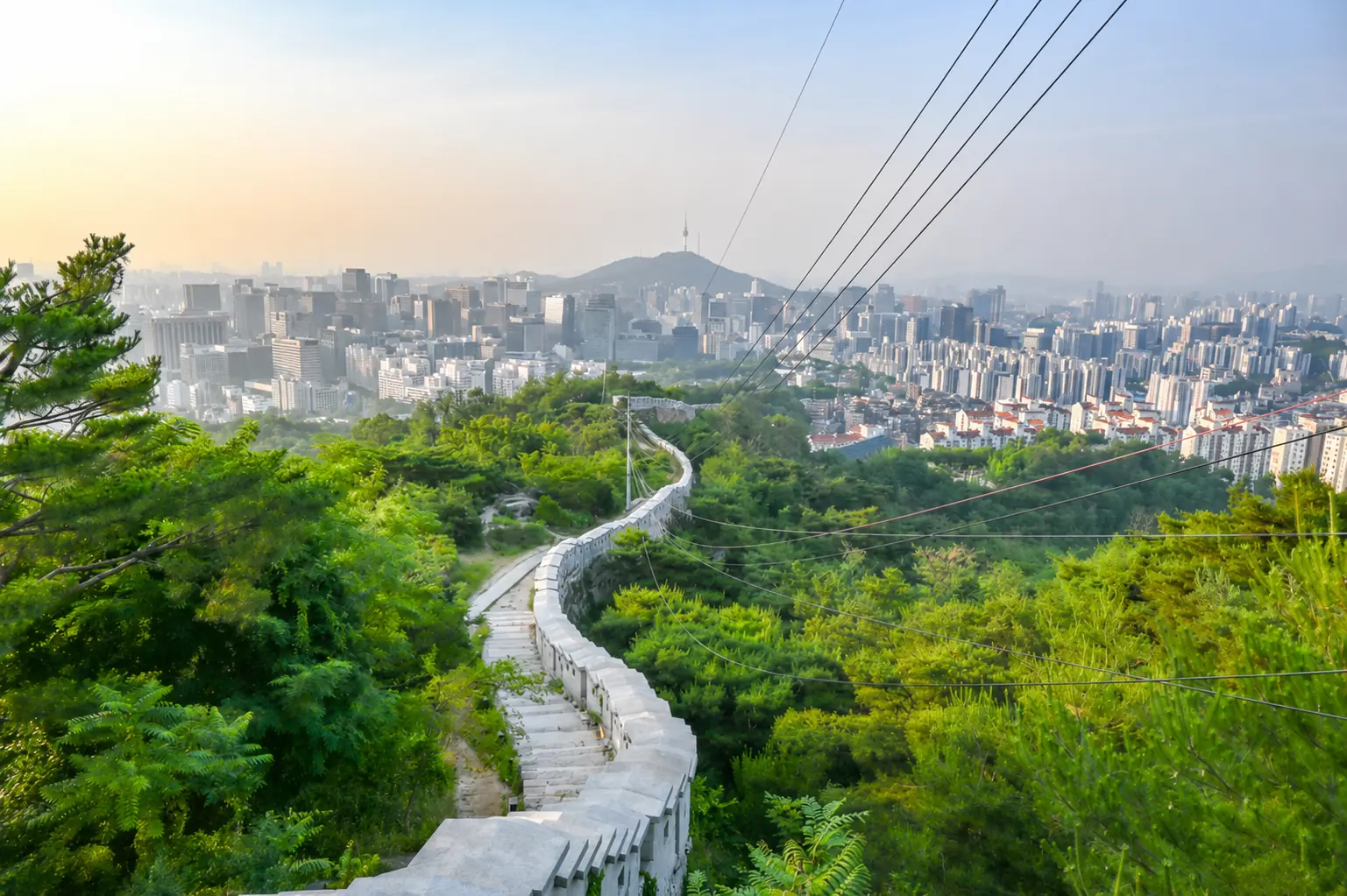 The city wall path curving down a wooded ridge above the Seoul skyline