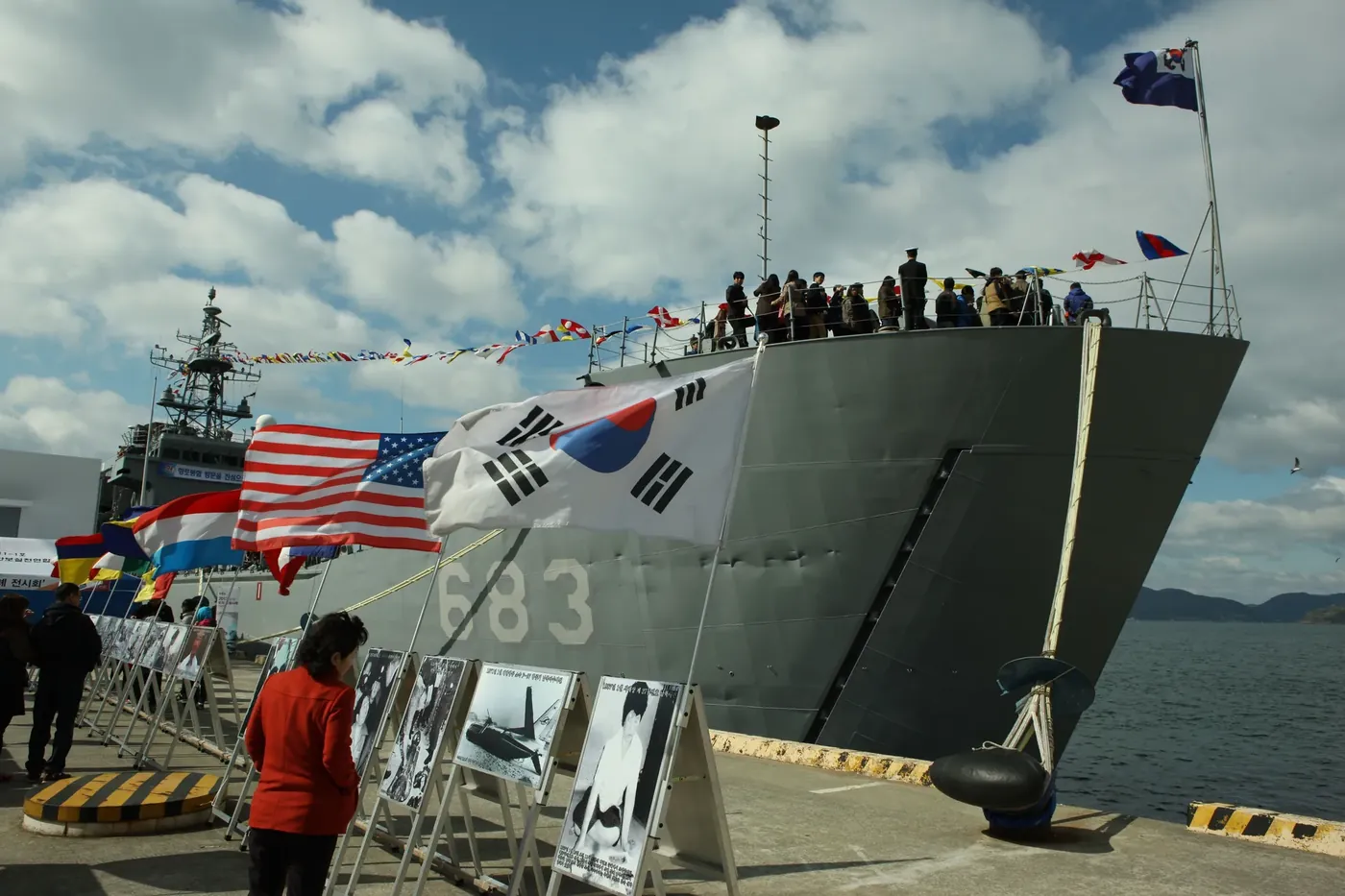 Naval ship bow with flags flying above visitors gathered on the quay