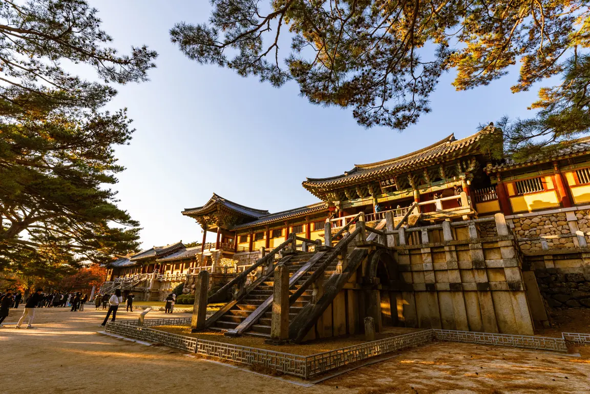 Visitors walking in a line across an open courtyard below a temple gate