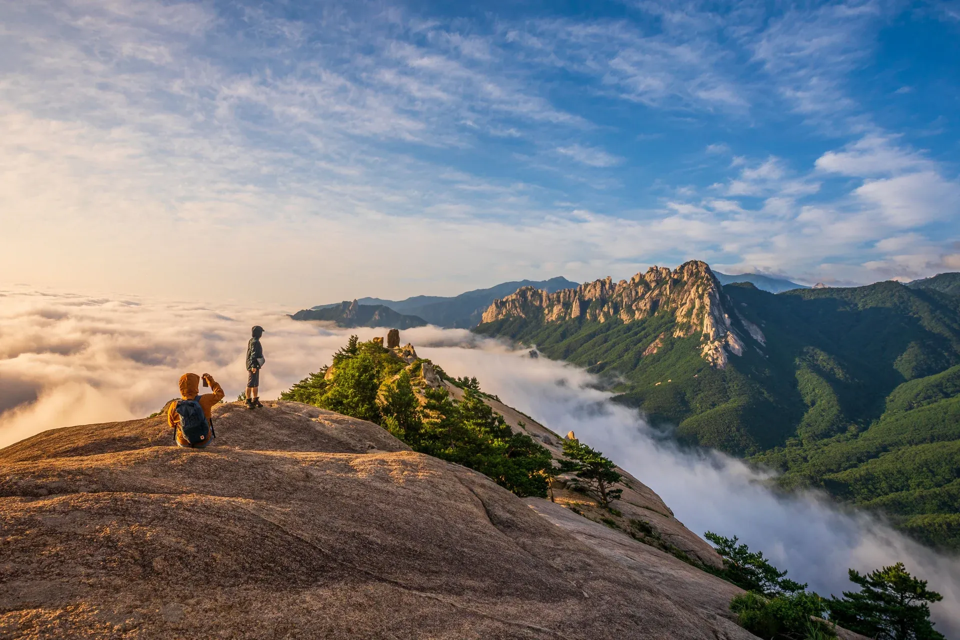 Two hikers on a granite summit above a sea of cloud
