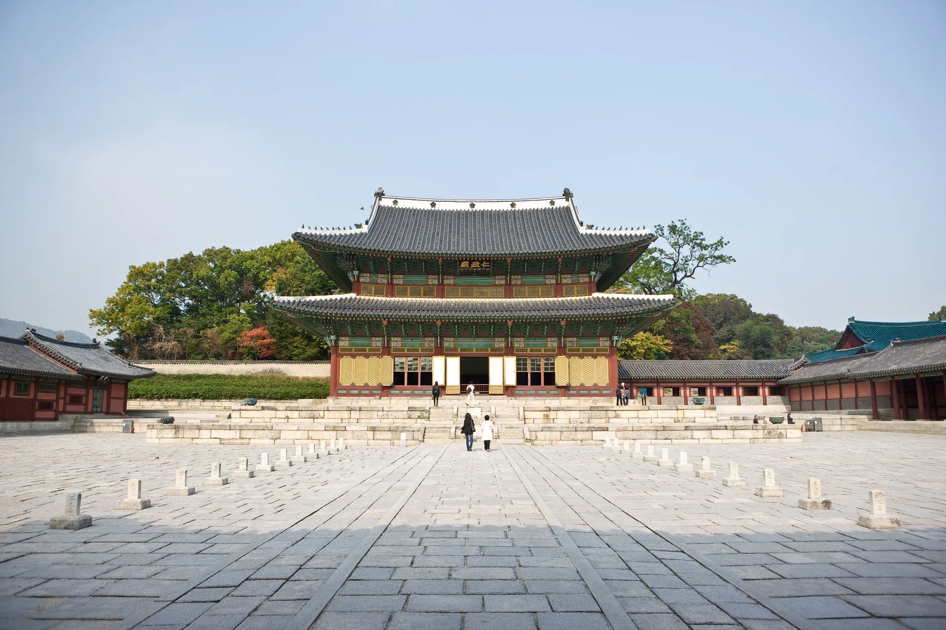 A two-tiered wooden hall facing a wide stone-paved courtyard enclosed by low corridors
