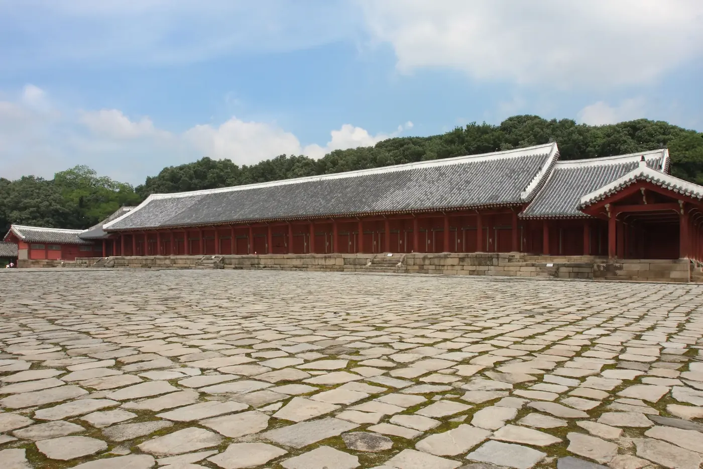 A long tiled-roof hall on a raised platform above a wide courtyard of rough stone slabs